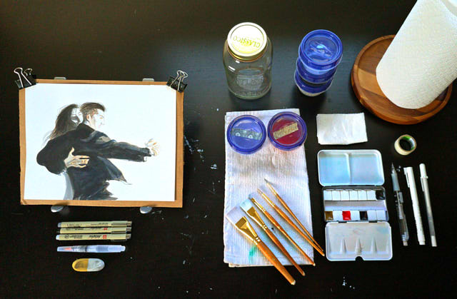 A spread of watercolor supplies, with a color painting towards the left.